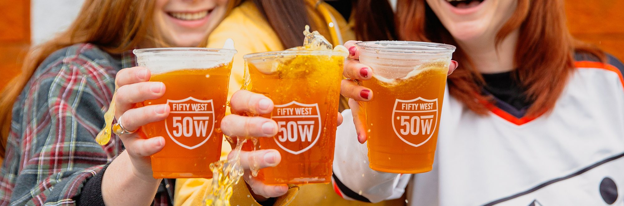 Friends cheersing Fifty West beers in front of the brewery
